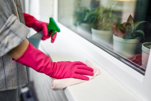 Person wearing pink gloves using a spray bottle to clean a windowsill